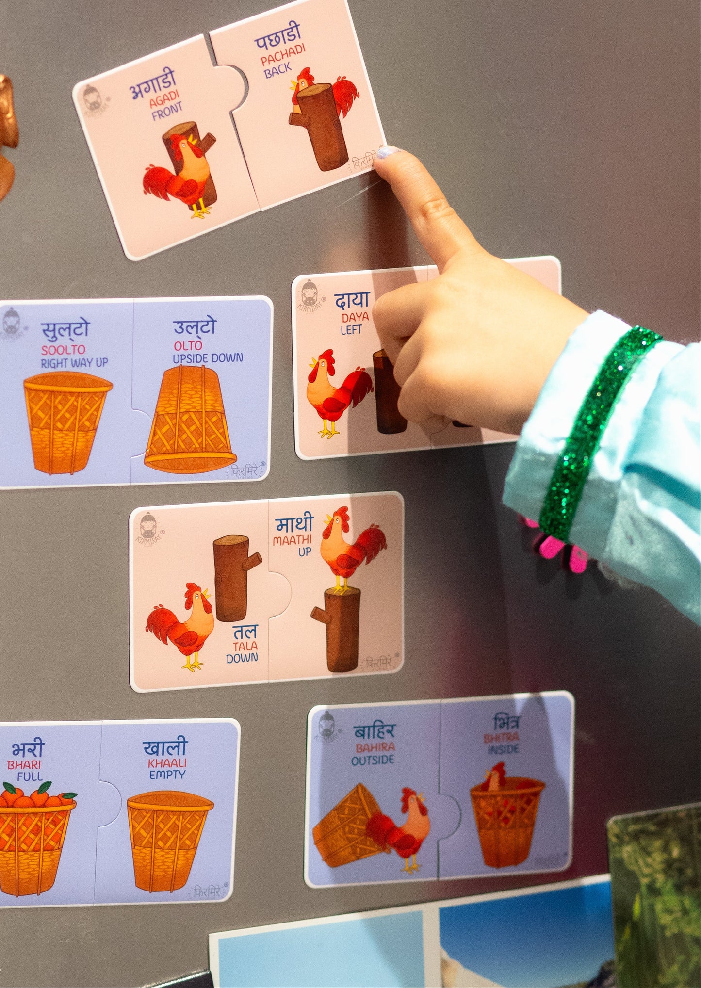 Child's hand interacting with fridge magnets with designs of Nepali English opposite words
